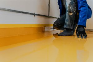 Worker coating floor with self-leveling epoxy resin in industrial workshop