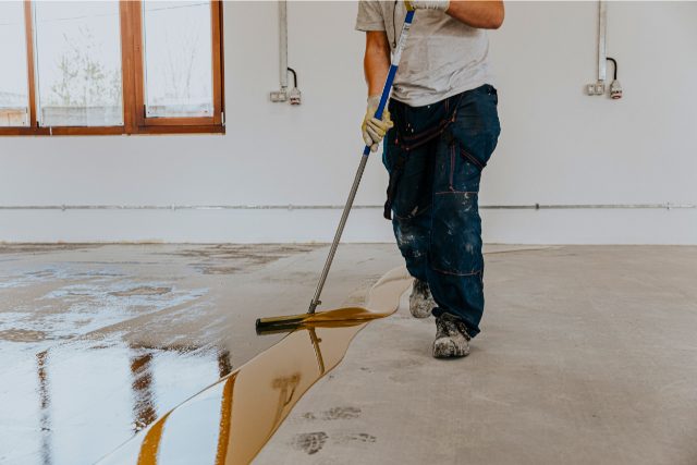 A worker applies the primer to the concrete floor